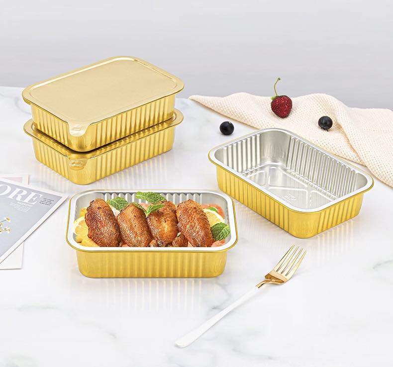 Nhiều chiếc khay nhôm nhỏ đang được một đầu bếp chia suất ăn (meal prep) một cách chuyên nghiệp. Mỗi khay đều trông rất hấp dẫn và khoa học.